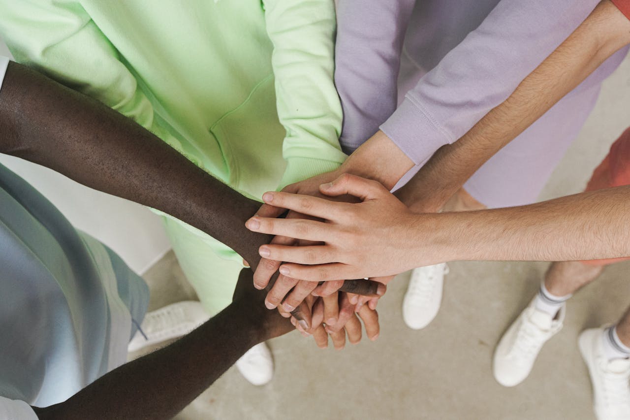 home-hero Top view of diverse hands stacked together, symbolizing unity and teamwork.